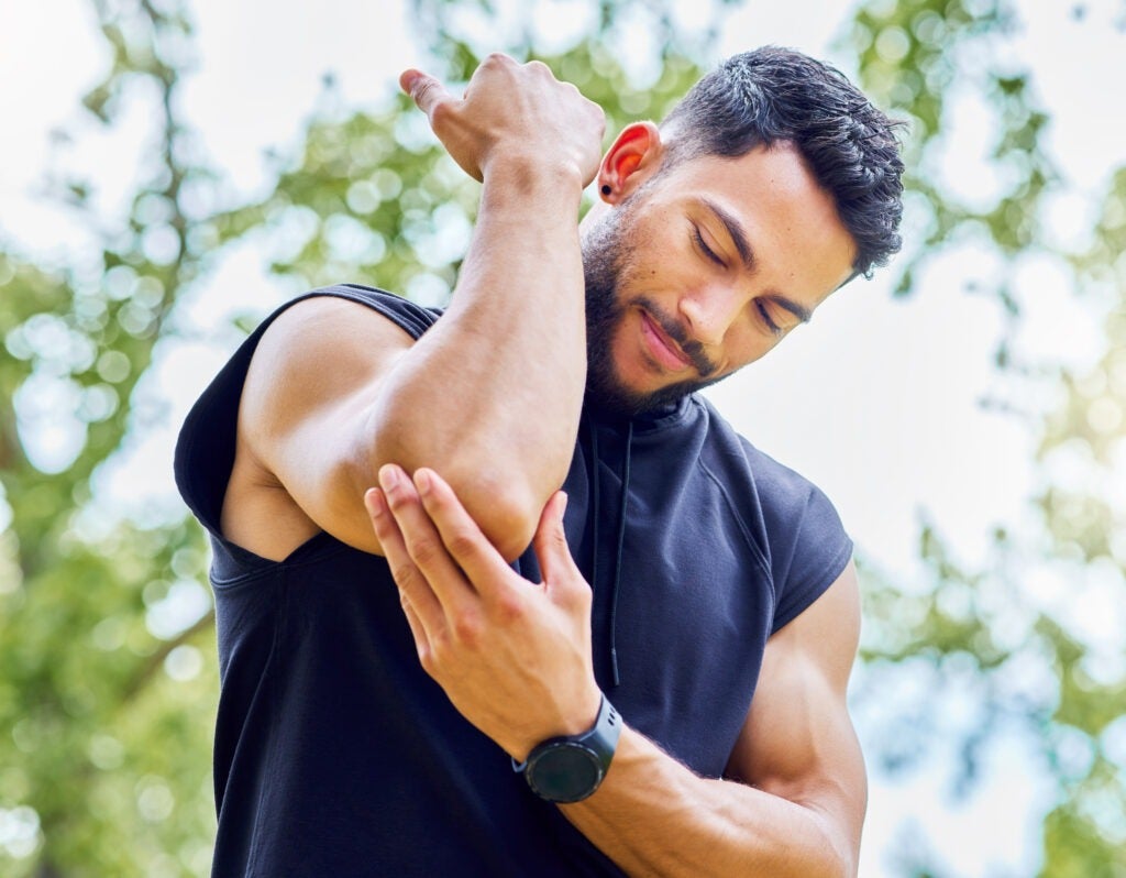 Low angle shot of a sporty young man experiencing elbow pain while exercising outdoors