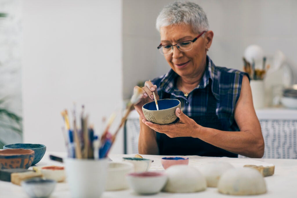 Senior woman decorating bowl made of clay on ceramics workshop.