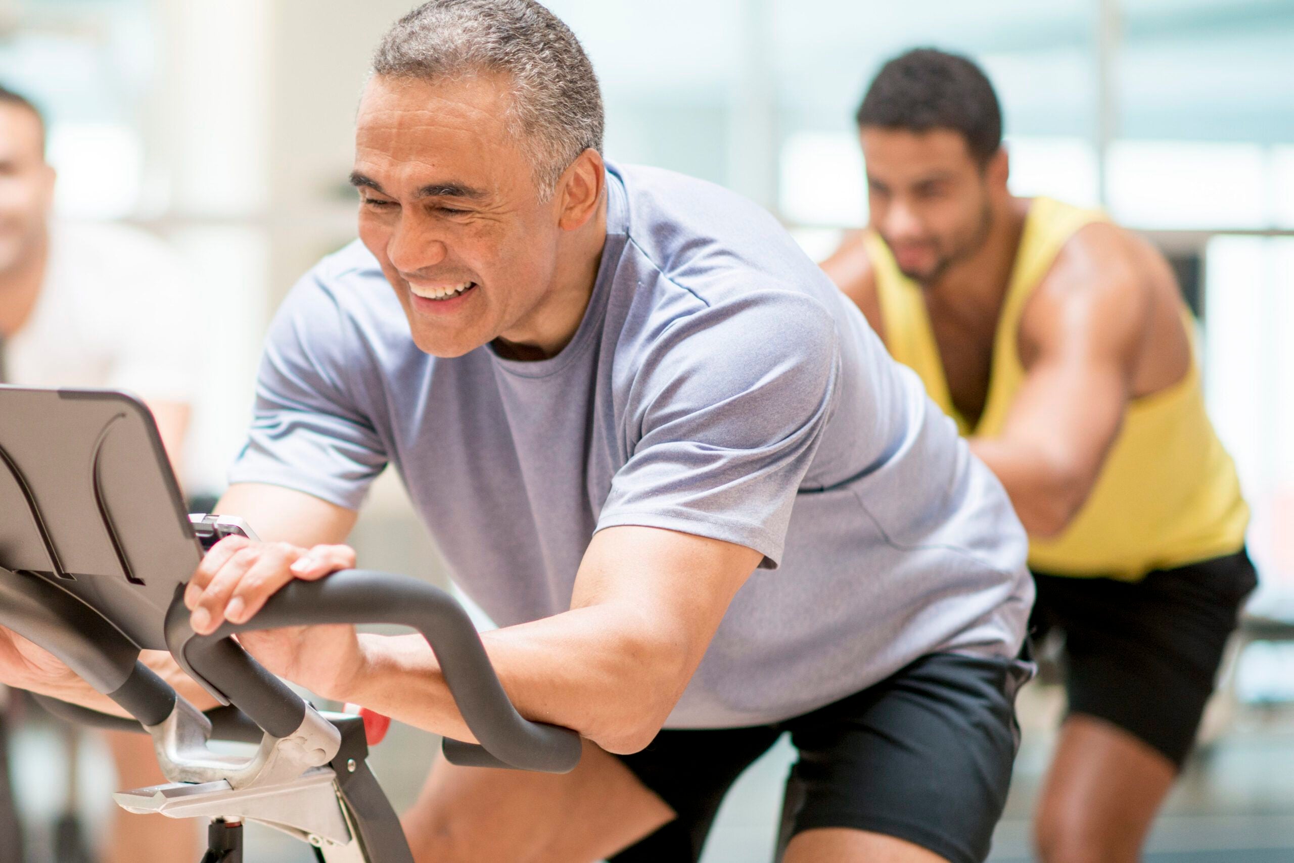 adults are taking a exercise class together at the gym. They are working by cycling on stationary bikes.